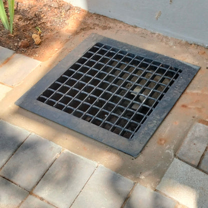 Metal drain cover on a paved pathway with plants around